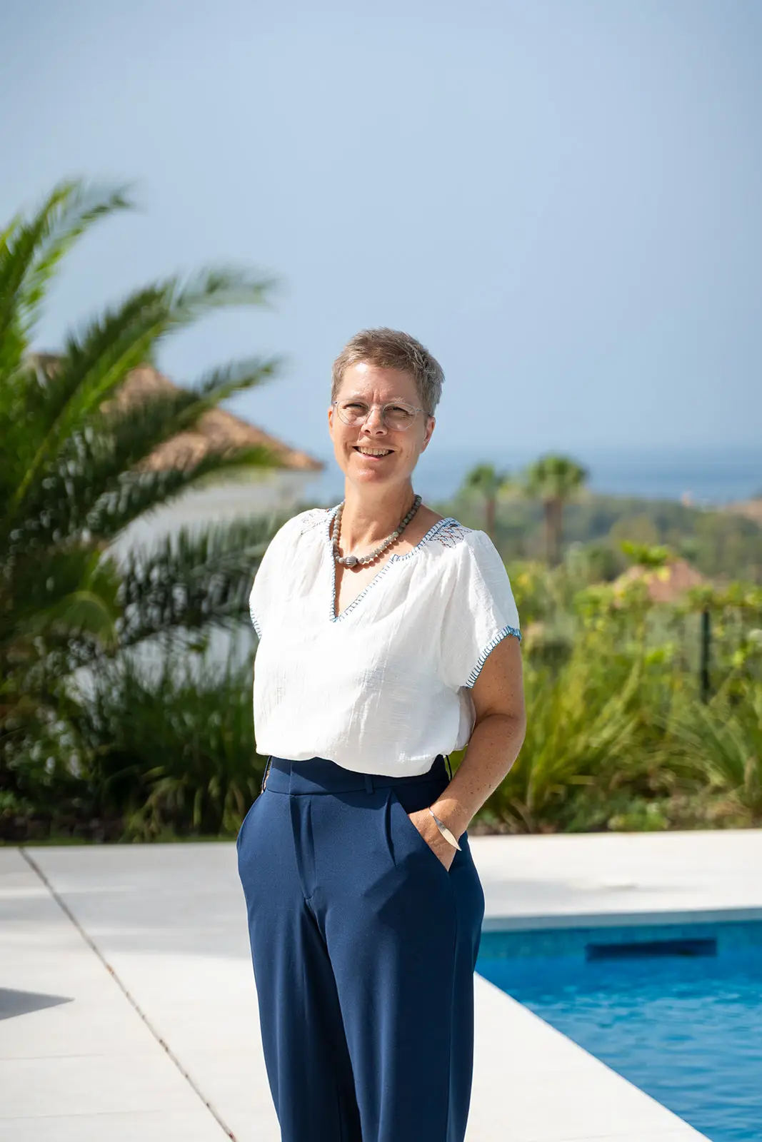 Mette standing on the terrace with palm trees and the coast behind her