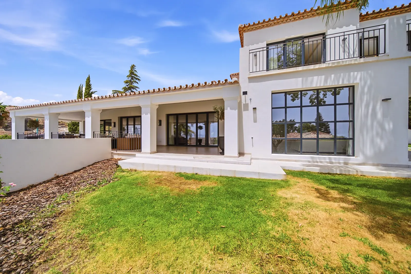 White villa with terracotta roof tiles seen across a lawn